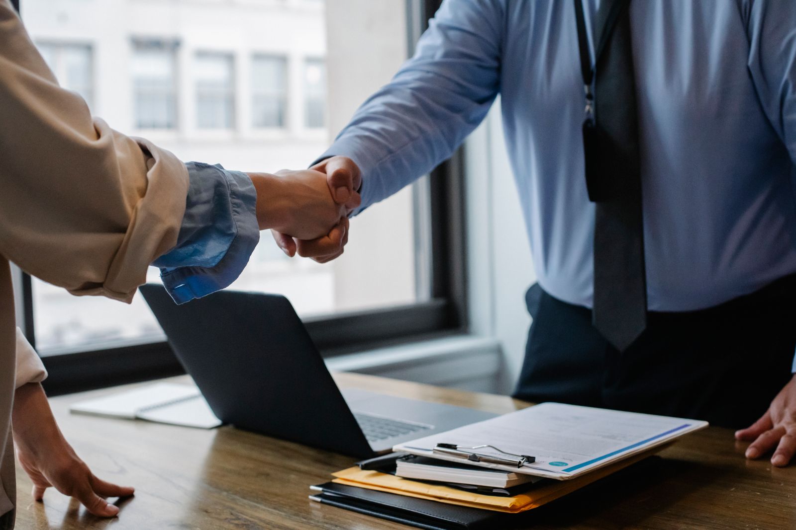 Two people shaking hands over a desk after a meeting