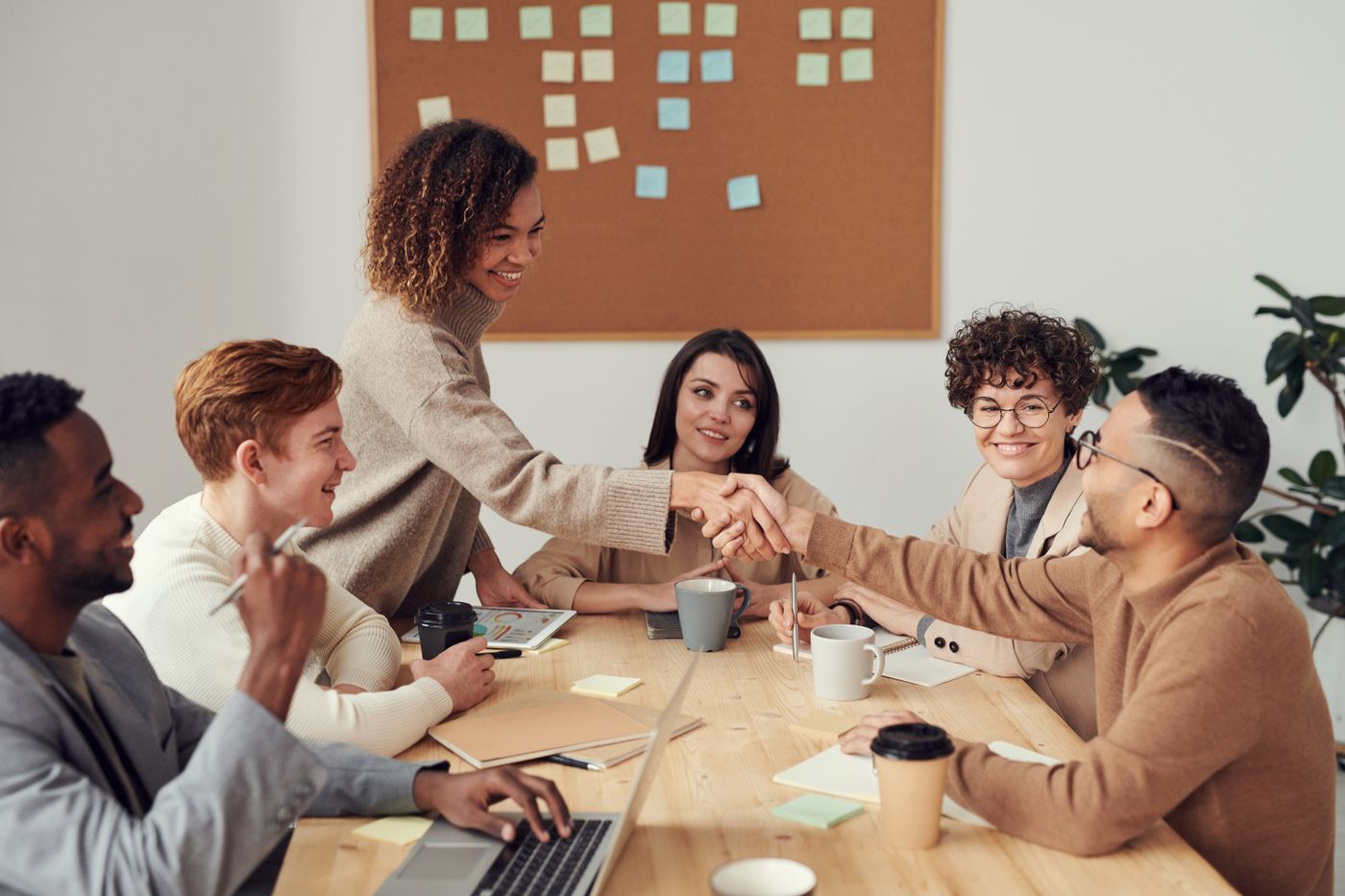 Colleagues shaking hands across a meeting table while a team looks on