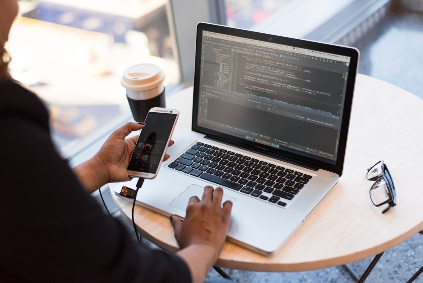 A person holding a phone beside an open laptop at a desk